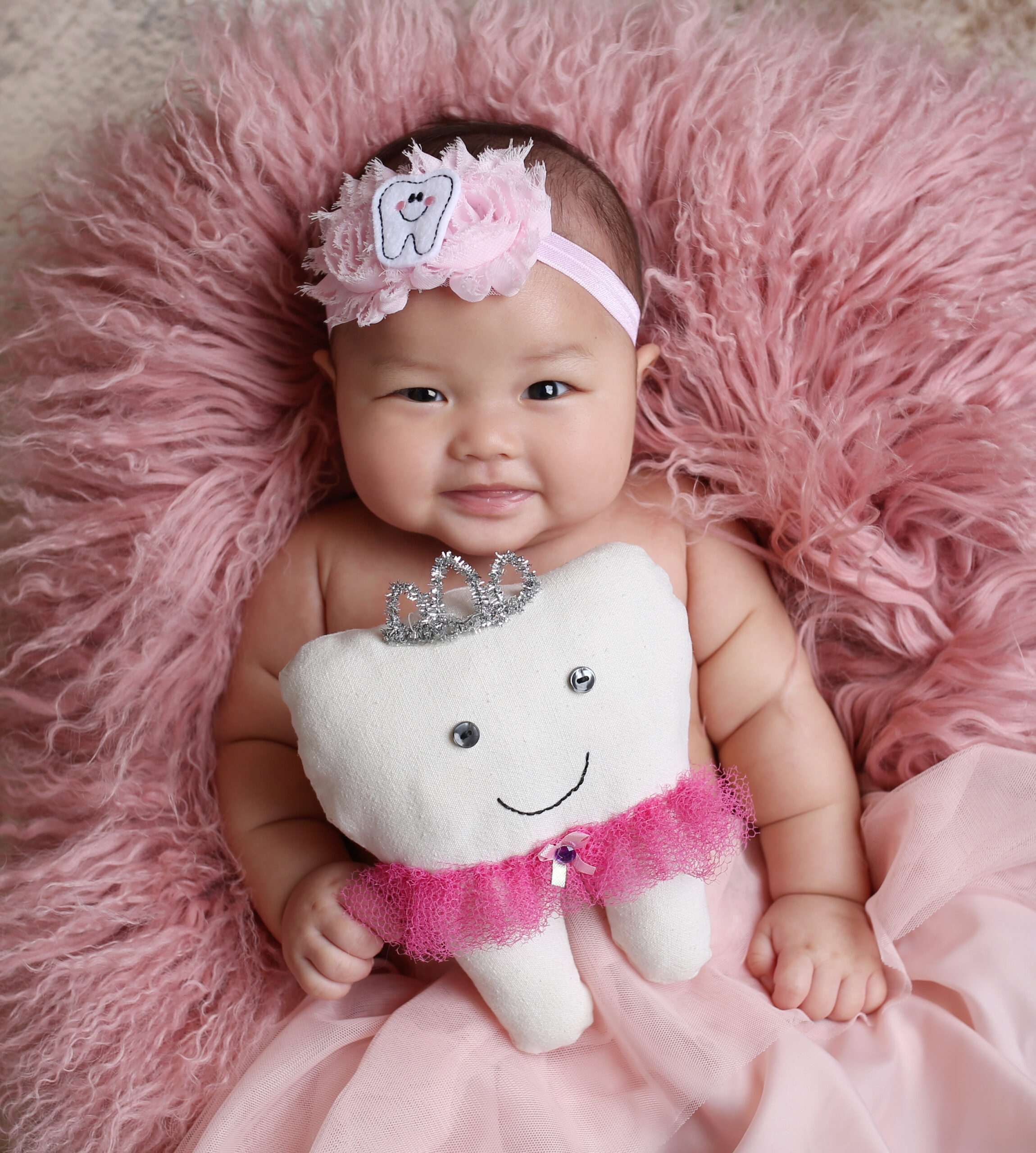 Smiling baby with a plush tooth pillow — Giggles & Grace Pediatric Dentistry